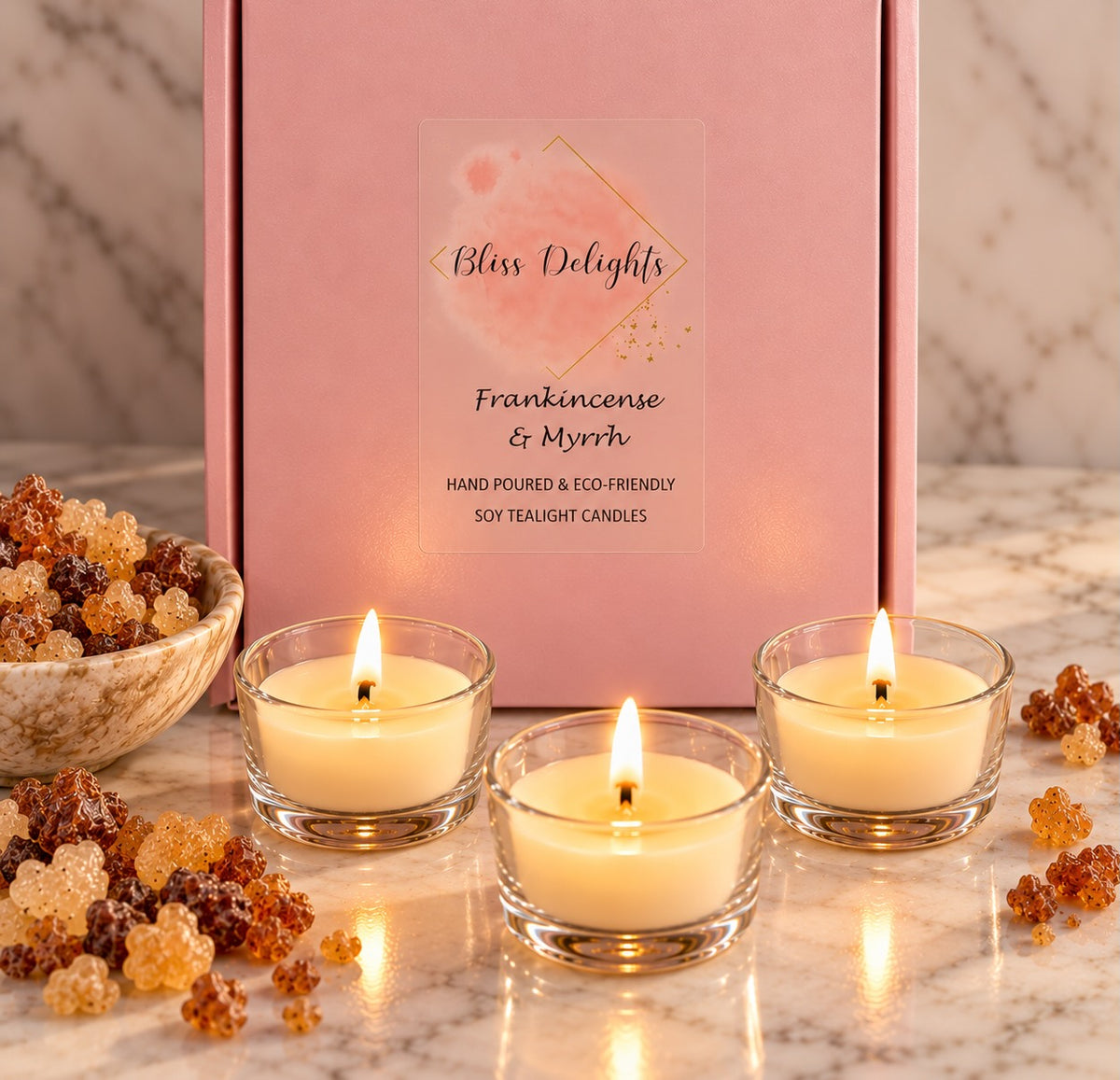 Bliss Delights Frankincense & Myrrh soy tealight candles in a pink gift box with a transparent label, styled with glowing tealights, amber resin pieces and a marble background.