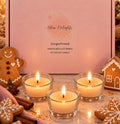 Bliss Delights Gingerbread soy tealight candles in a blush-pink gift box with a branded label, styled with three glowing tealights in clear glass holders, iced gingerbread cookies, cinnamon sticks and star anise.