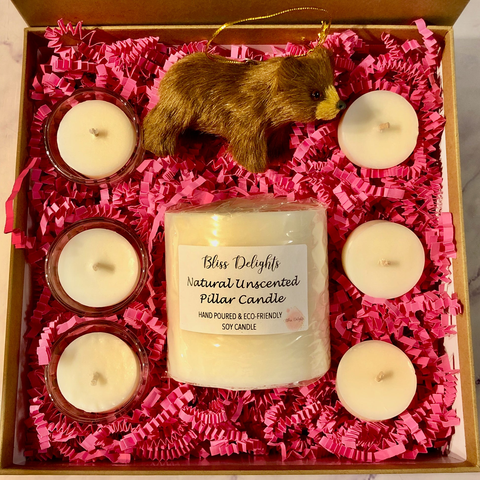 Gift set with candles and a bear figurine on pink crinkled paper