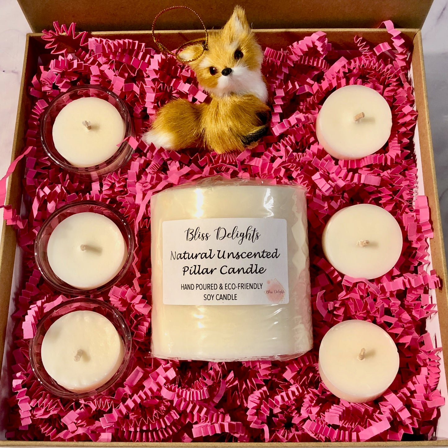 Gift set with candles and a fox figurine in a box lined with pink tissue paper.