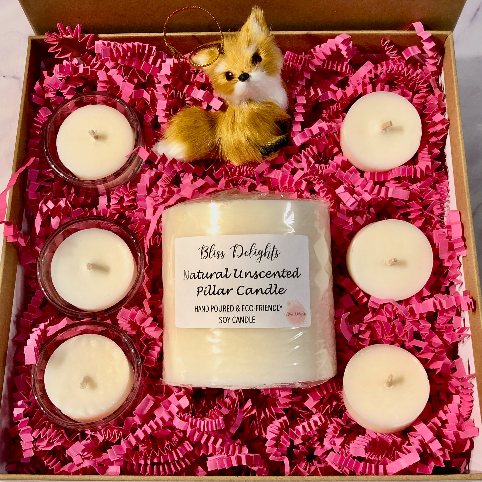Gift set with candles and a fox figurine in a box lined with pink tissue paper.