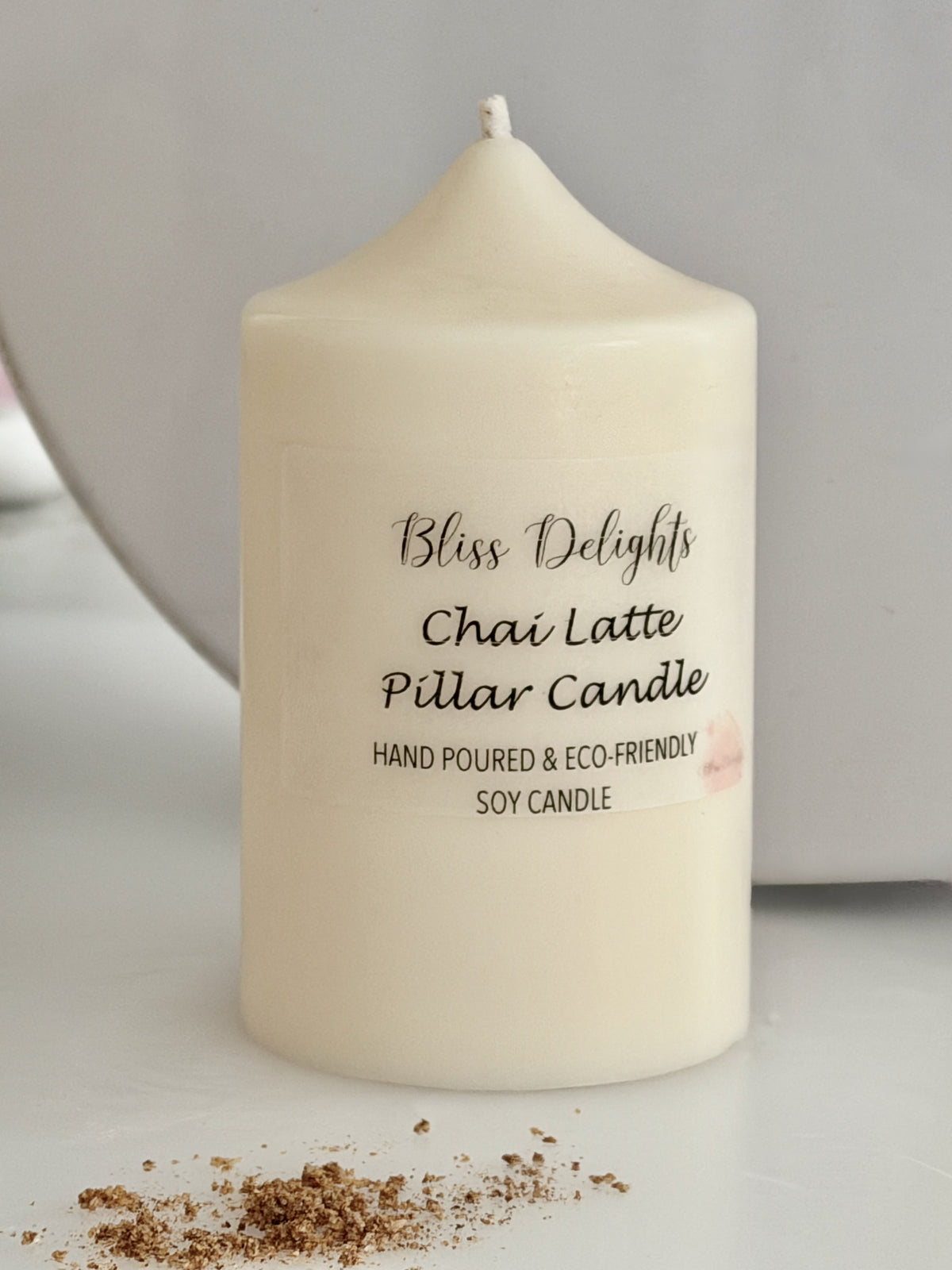 Cream soy wax pillar candle by Bliss Delights, labelled Chai Latte, photographed on a white surface with brown sugar scattered nearby.