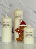 Three cream-coloured Bliss Delights Gingerbread soy wax pillar candles in small, medium and large sizes, arranged with a festive gingerbread figure wearing a Santa hat and holding a candy cane, against a white marble background.