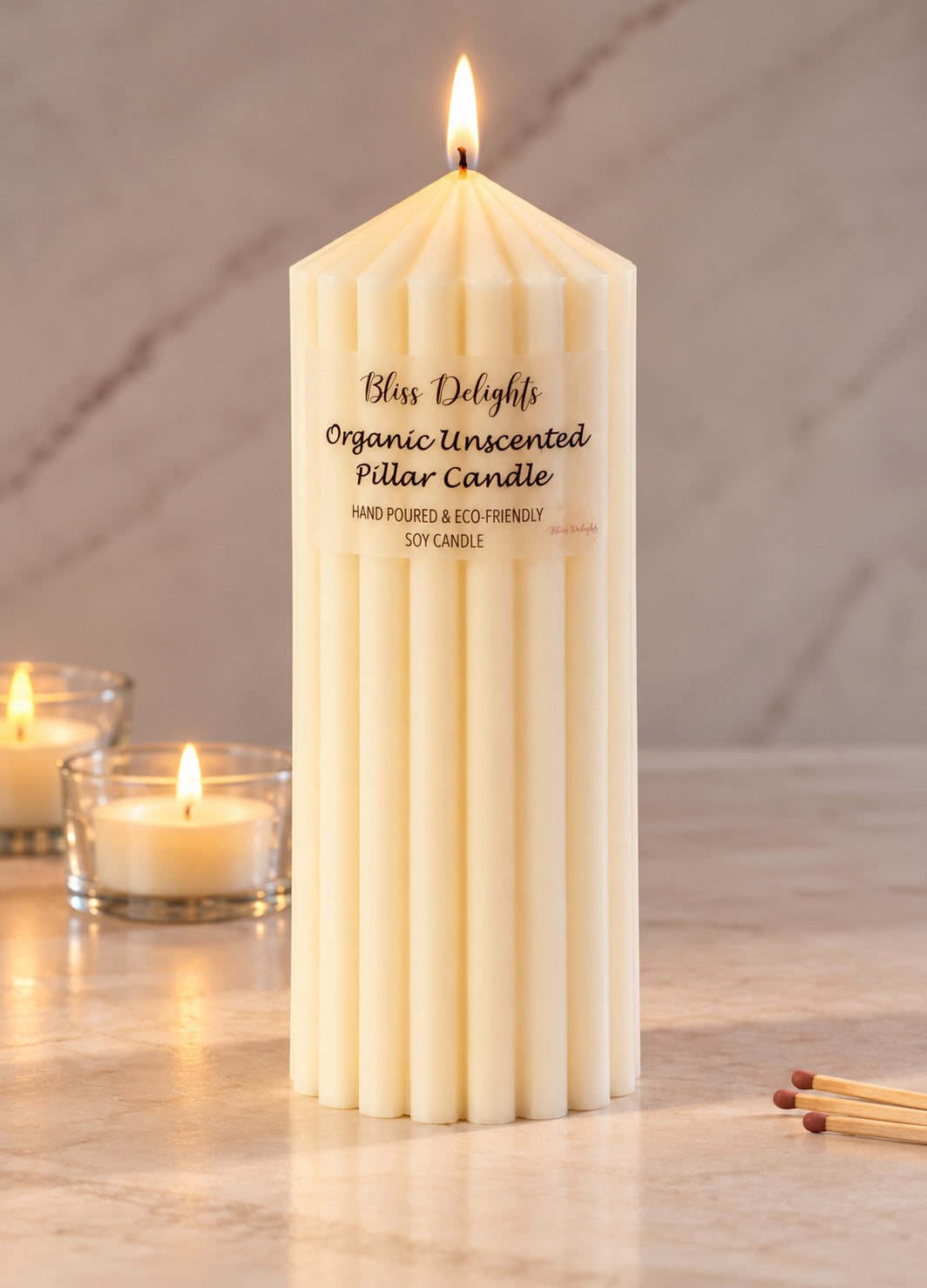 Bliss Delights Large Organic Soy Pillar Candle with matches and soy tealights in glass holders in the background.