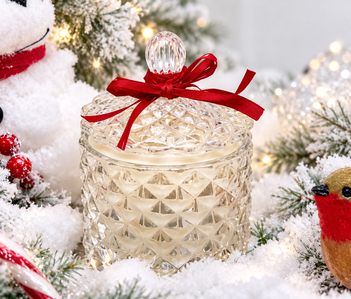 Bliss Delights pearlescent diamond soy candle in a faceted glass jar with a red ribbon, styled with snowy foliage, warm fairy lights and festive Christmas decorations.