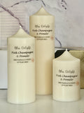 Three cream-coloured Bliss Delights Pink Champagne & Pomelo soy wax pillar candles in small, medium and large sizes, arranged against a white marble background with gold gift packaging behind them.
