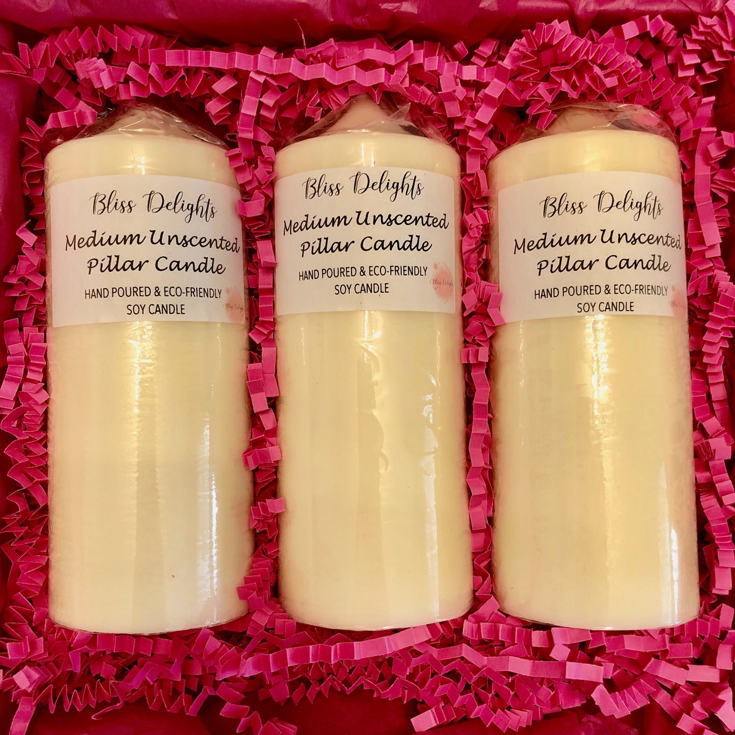 Bliss Delights three medium unscented pillar candles in a box with pink crinkled paper