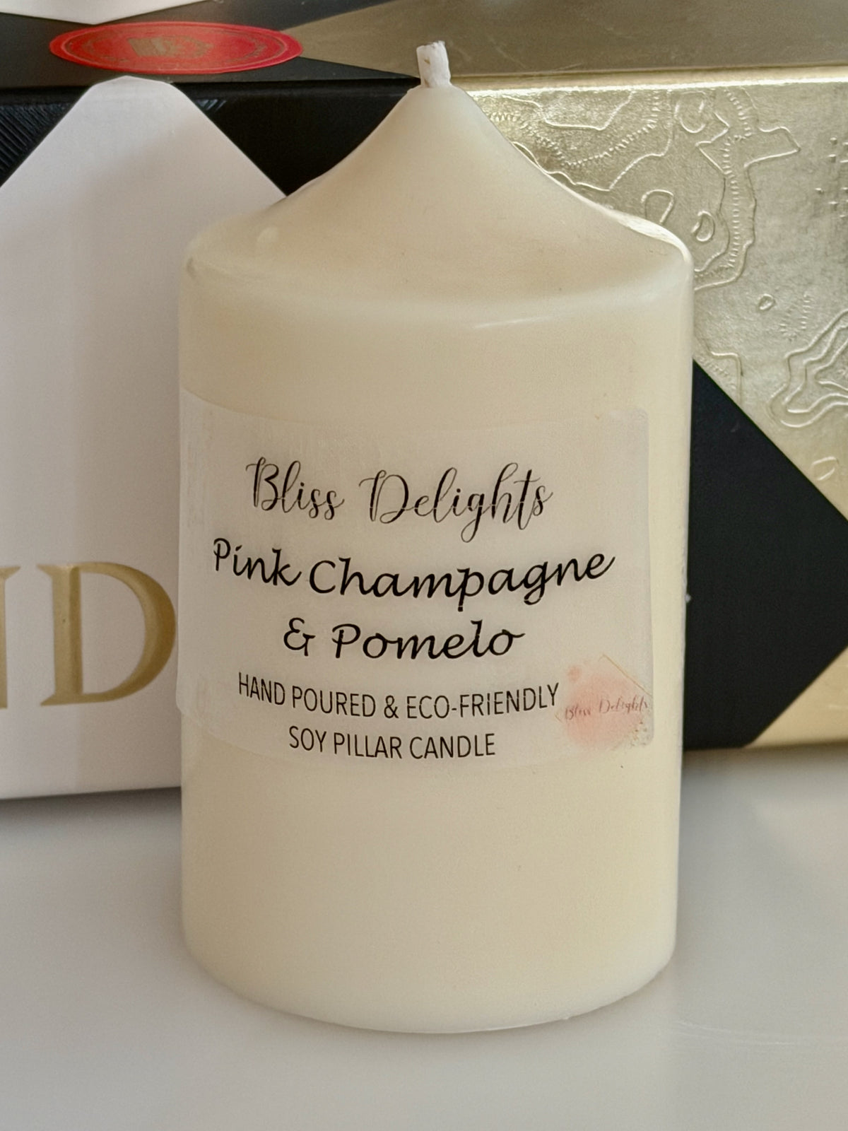 Ivory soy wax pillar candle by Bliss Delights, labelled Pink Champagne & Pomelo, displayed beside decorative gift packaging.