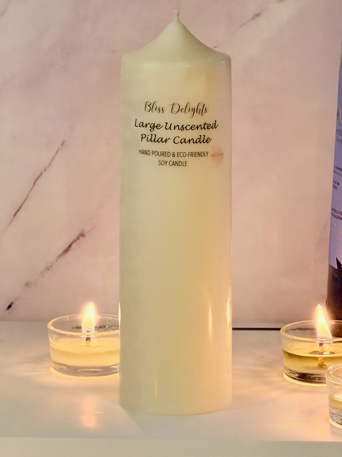 Large ivory soy wax pillar candle by Bliss Delights, photographed with glowing tealights against a pale marble background.